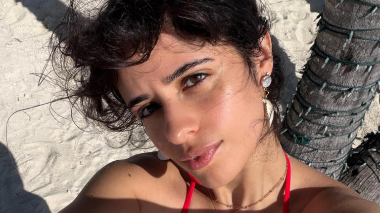 Camila Cabello walking along a sandy beach in natural light, appearing relaxed and confident during a seaside outing.