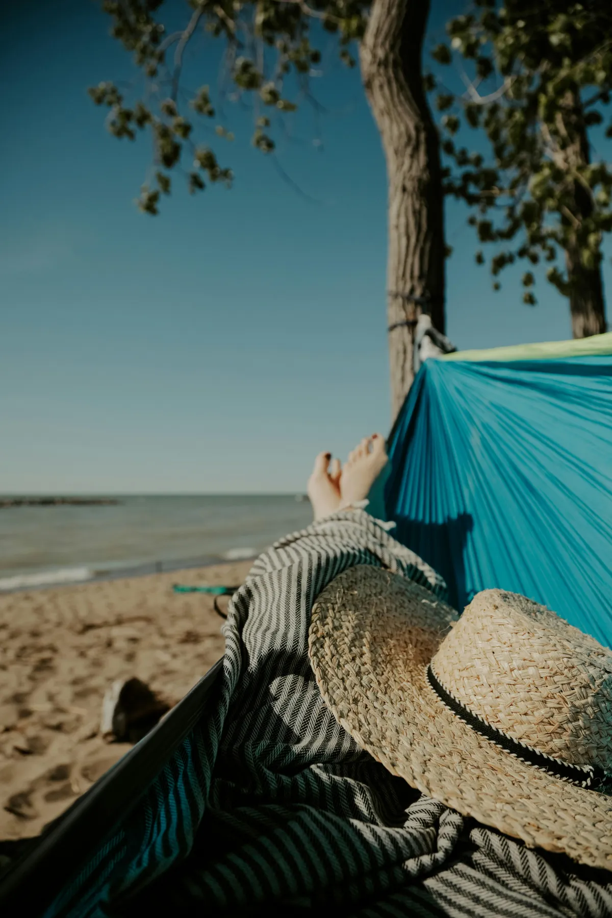 View of a person's legs in a hammock with the beach in the background