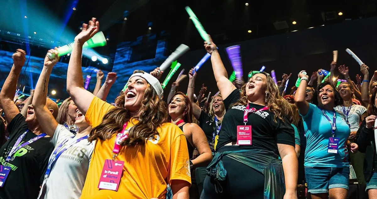 A group of energized women at a live Momentum Pro event cheering with glow sticks, wearing name badges and event shirts, celebrating empowerment and community.