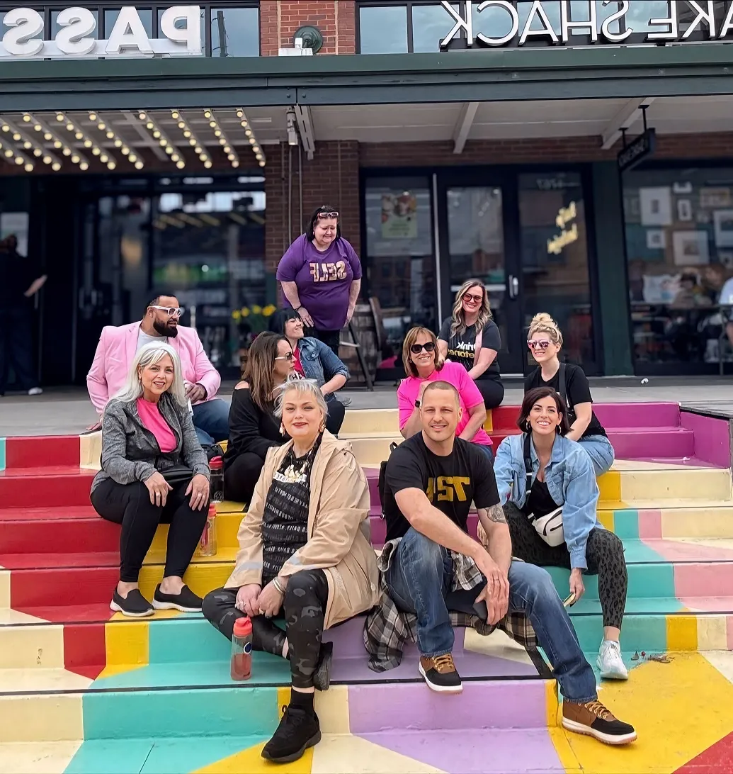 A colorful group of entrepreneurs and leaders from Momentum Pro gathered on rainbow-painted stairs in front of Shake Shack, radiating unity, creativity, and fun.