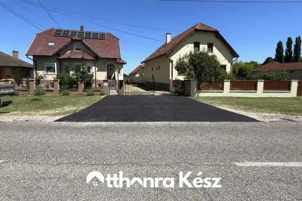 Széles, frissen aszfaltozott kocsibeálló csatlakozás egy családi ház bejáratánál.