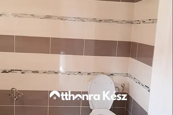 Modern fürdőszoba burkolás bézs és barna csempékkel, dekoratív mozaik csíkkal.
