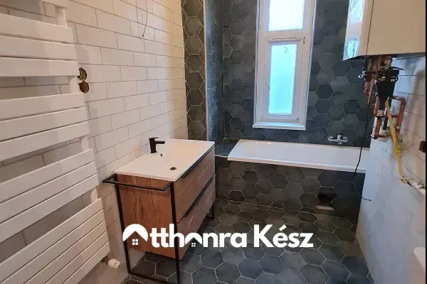 Modern fürdőszoba sötét hatszögletű (méhsejt) burkolattal, fehér metro csempével és fa-fém mosdószekrénnyel.