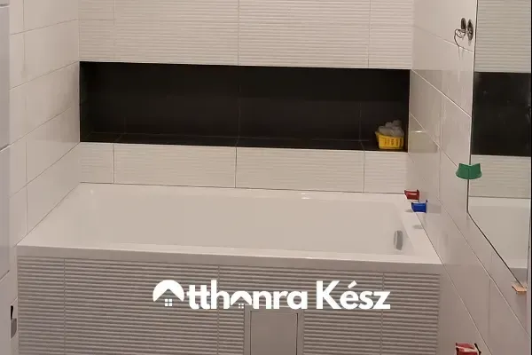 Modern fürdőszoba felújítás fekete-fehér csempével, beépített káddal és épített falfülkével.