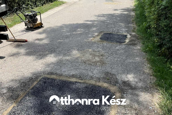 Sérült aszfaltfelület javítás előtt, kátyúkkal és repedésekkel egy keskeny útszakaszon