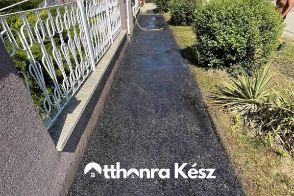 Keskeny, frissen aszfaltozott bejáró kerítés és kertszegély mellett, tartós fekete aszfalt felülettel