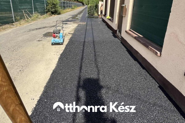 Keskeny udvari aszfaltjavítás frissen lerakott fekete aszfalttal, szegély mellett és gépi előkészítéssel