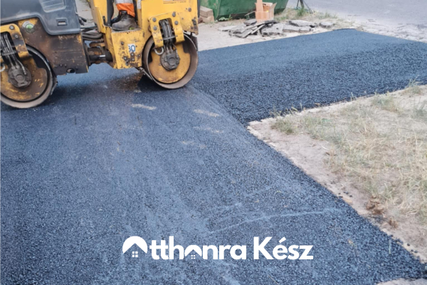 Gépi aszfaltozás frissen terített fekete aszfalt felülettel, hengerrel tömörítve egy udvari útszakaszon