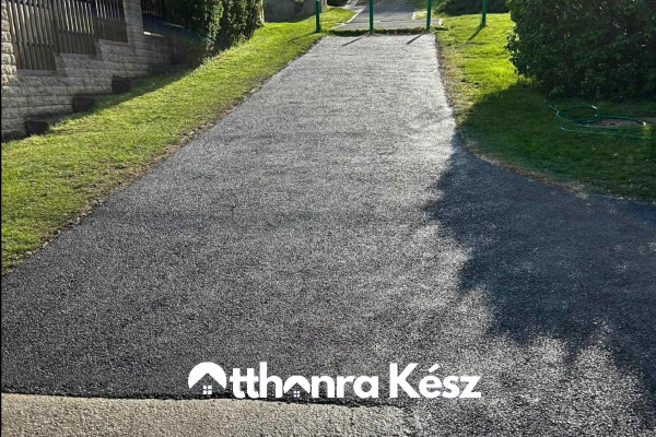 Gépi aszfaltozás keskeny kapubejárón, frissen terített fekete aszfalt felülettel és pontos szegélyezéssel
