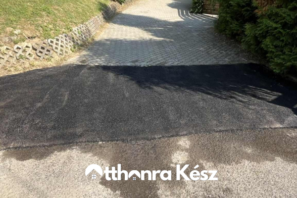 Frissen aszfaltozott lejtős bejáró és felhajtó, két burkolat találkozásával és tartós fekete aszfalt felülettel