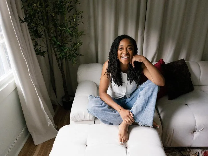 Woman sitting barefoot on a white couch smiling warmly