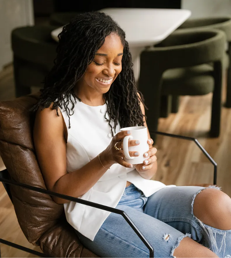Woman smiling while holding a mug seated comfortably in a modern chair