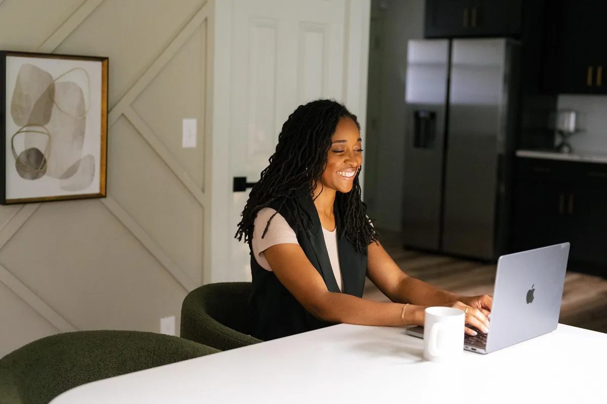 Smiling woman working on a laptop at a kitchen table
