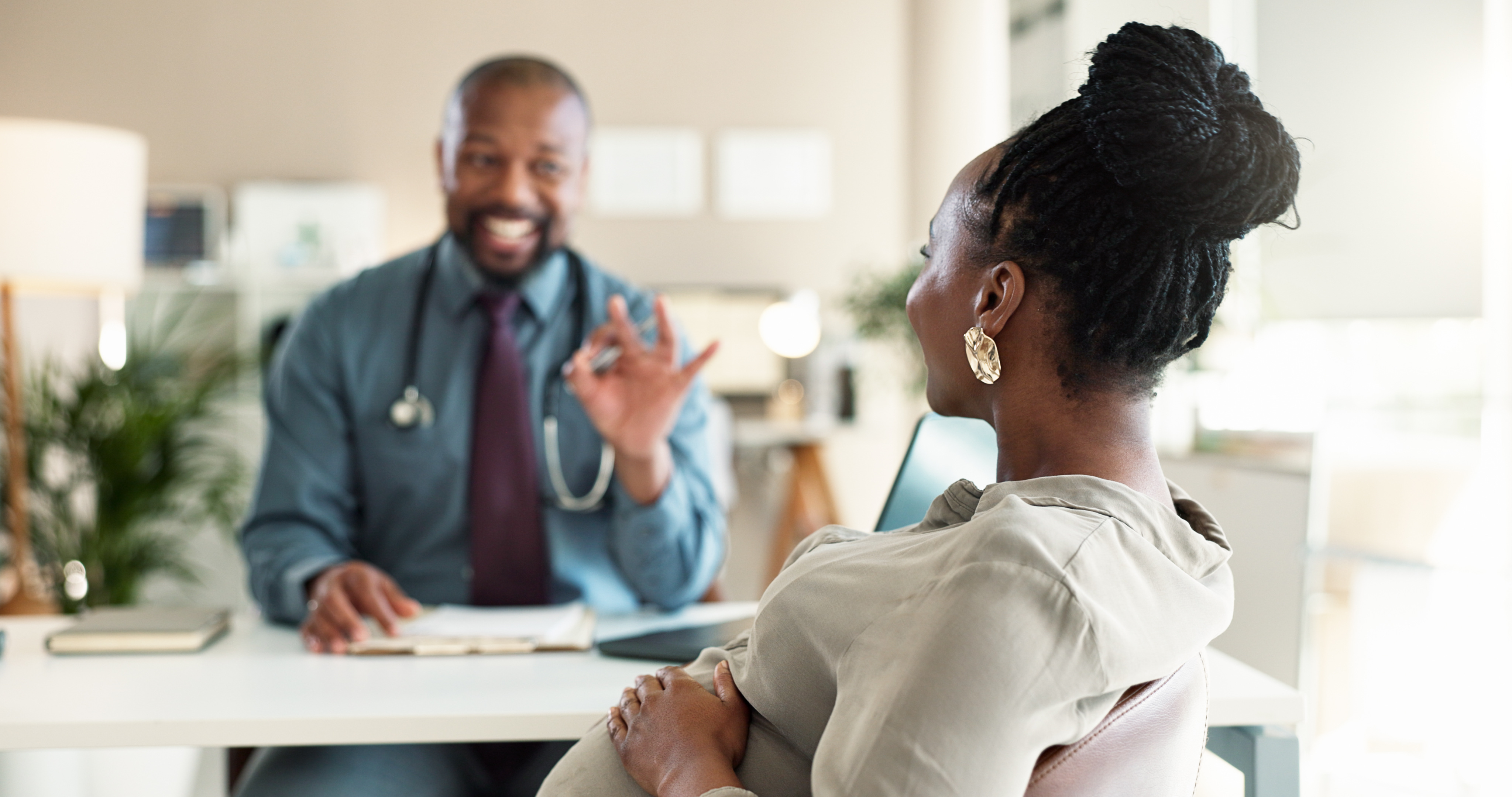 A doctor with a stethoscope talks to a patient in a medical office, both seated and facing each other.
