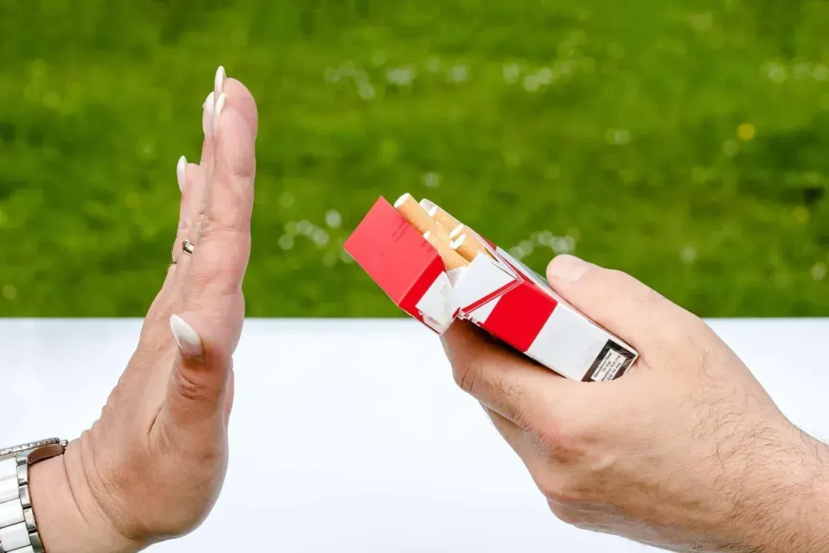 Hand gesturing stop to a pack of cigarettes in an outdoor setting