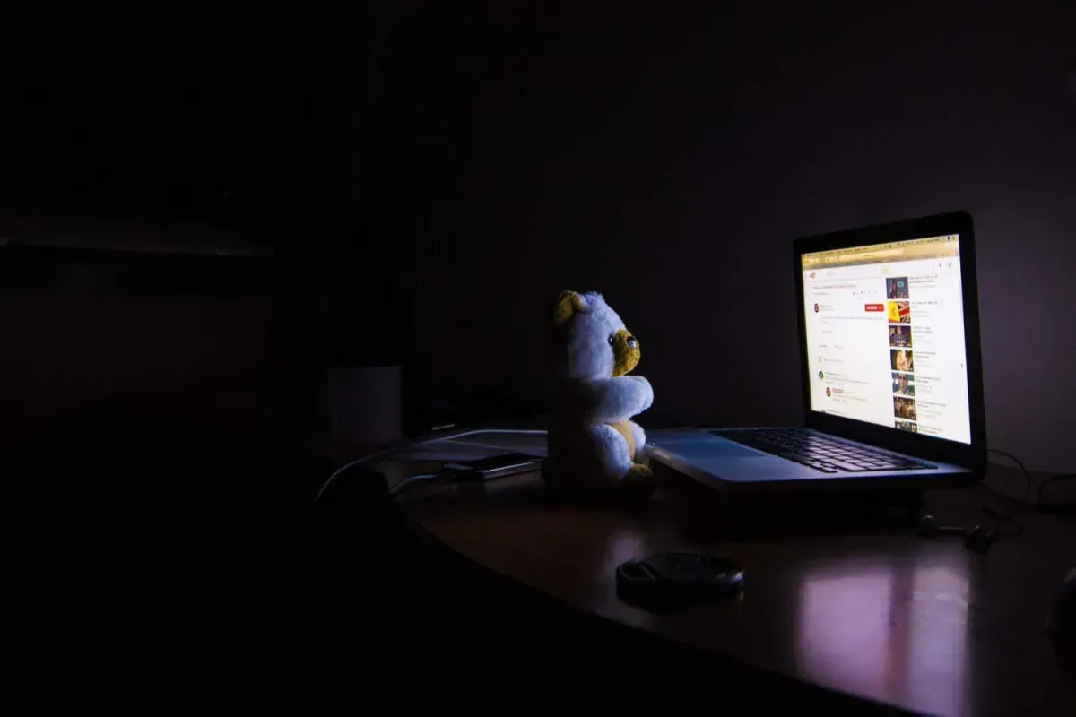 Teddy bear sitting in front of a laptop in a dark room