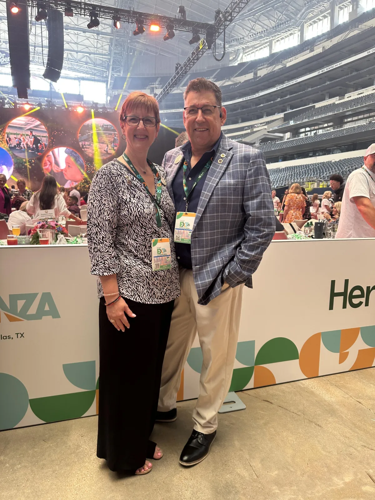 A confident woman in her late 20s stands outdoors, holding a phone and smiling as she prepares for a video call. The background is softly blurred greenery, and she wears casual, bright clothing. The image conveys optimism, readiness, and the excitement of starting something new.