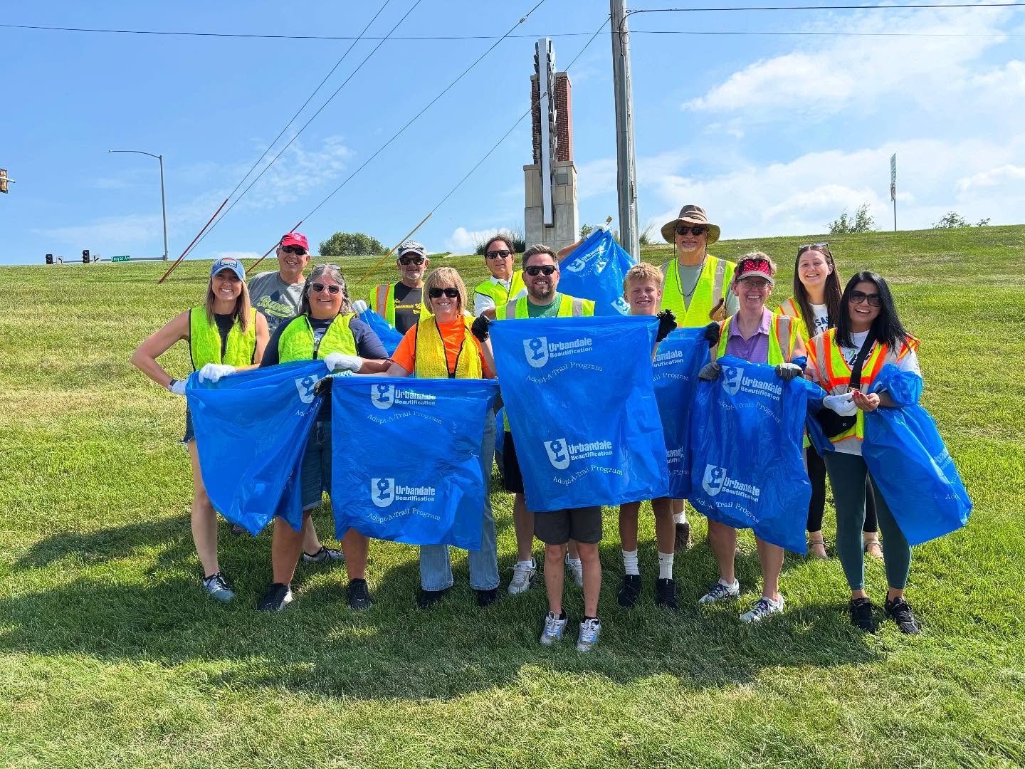 Group of volunteers in safety vests holding blue bags for a community cleanup event, promoting teamwork and environmental responsibility, relevant to job opportunities at Right Roofing & Siding.