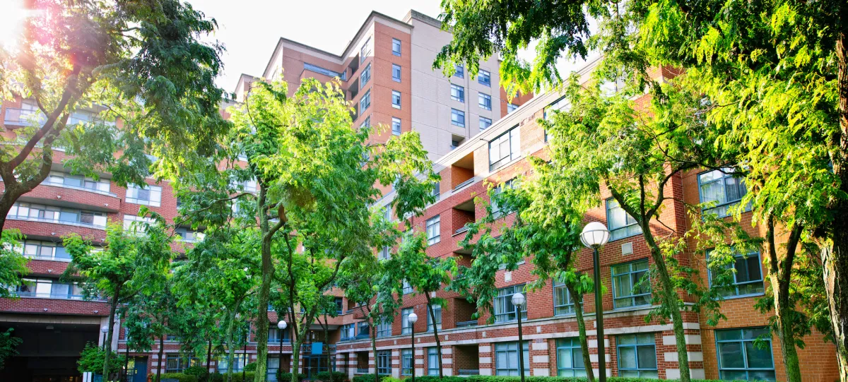 Multi-unit residential building surrounded by lush greenery, showcasing a mix of brick and modern architecture, relevant for roofing and siding services.