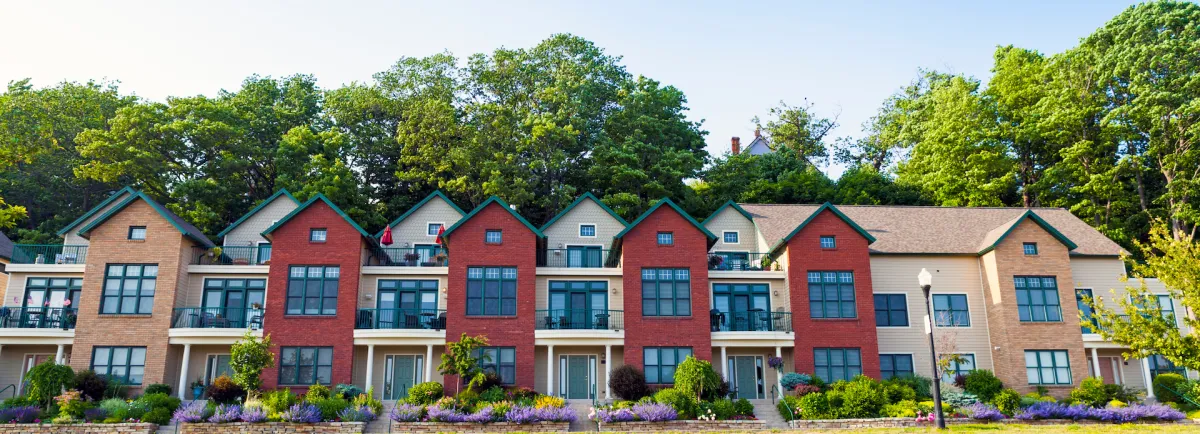 Townhouse community featuring multi-unit residential buildings with varied architectural styles, landscaped gardens, and a backdrop of lush trees, representing Right Roofing & Siding's exterior solutions for condos and townhouses in Central Iowa.