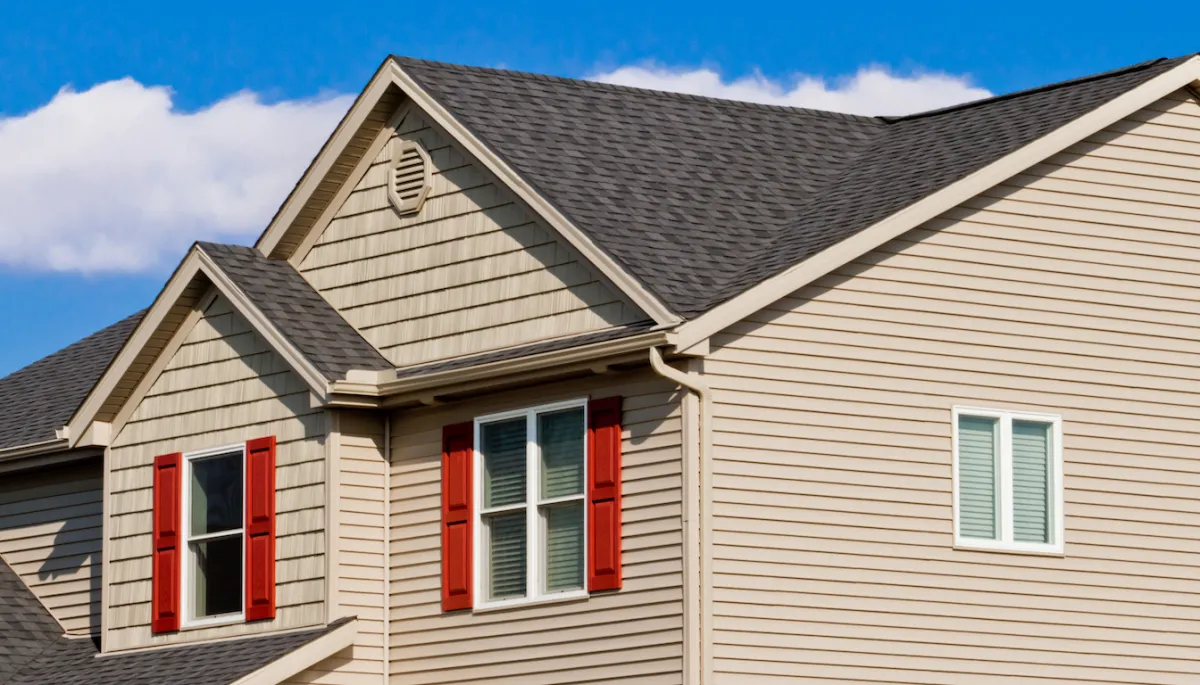 Residential home exterior featuring beige vinyl siding with red shutters and a gray shingled roof, illustrating durable siding options offered by Right Roofing for homeowners in Central Iowa.