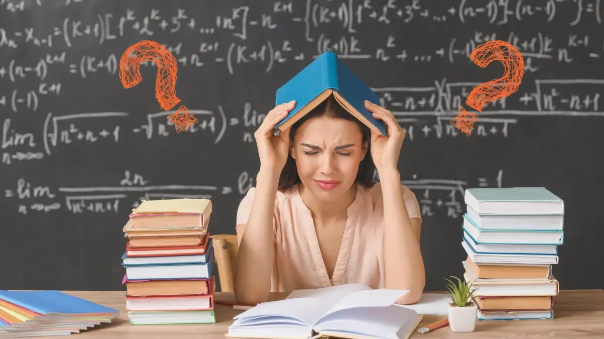 Stressed teacher with a book on her head surrounded by stacks of books and question marks in front of a classroom board