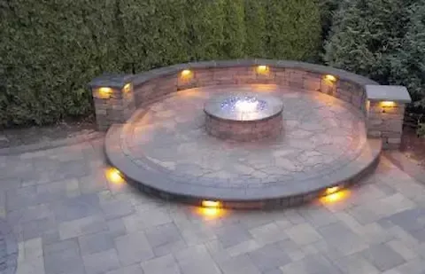 Circular stone patio with fire pit and lighting by Coastal Virginia Landscape & Design