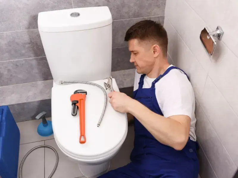 Plumber replacing a braided supply line behind a toilet, a common source of leaks behind the fixture