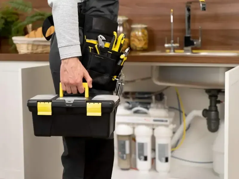 Plumber carrying toolbox past sink with water filtration system.
