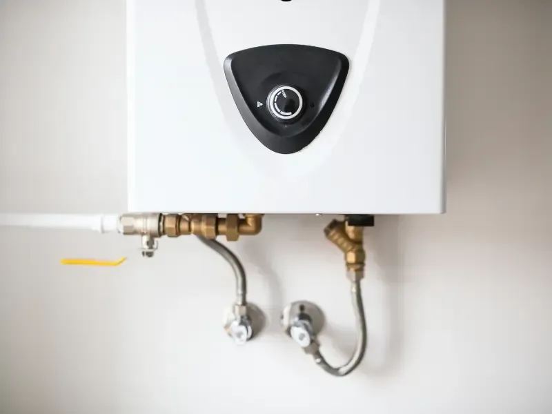 Close-up of a wall-mounted tankless water heater with connected gas and water isolation valves.