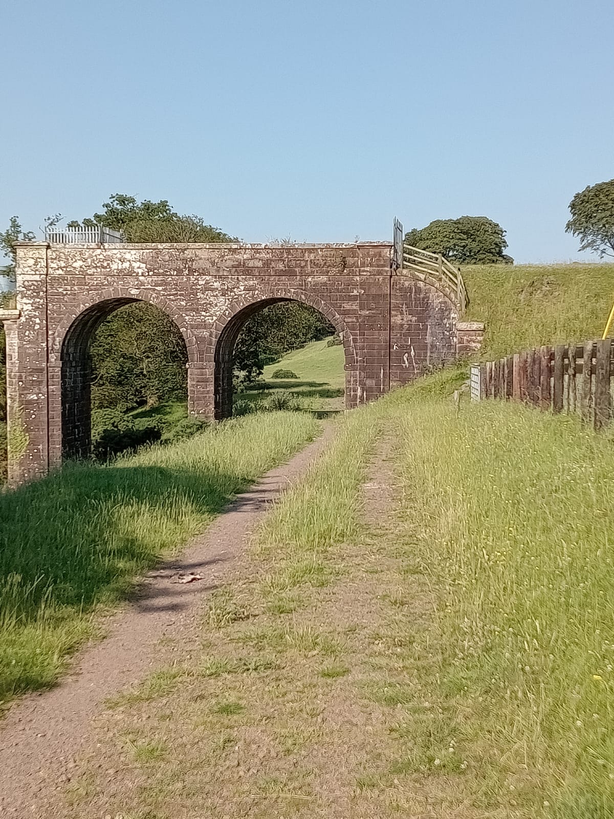 Grassy path leading towards the stone arches of Tongland Old Bridge