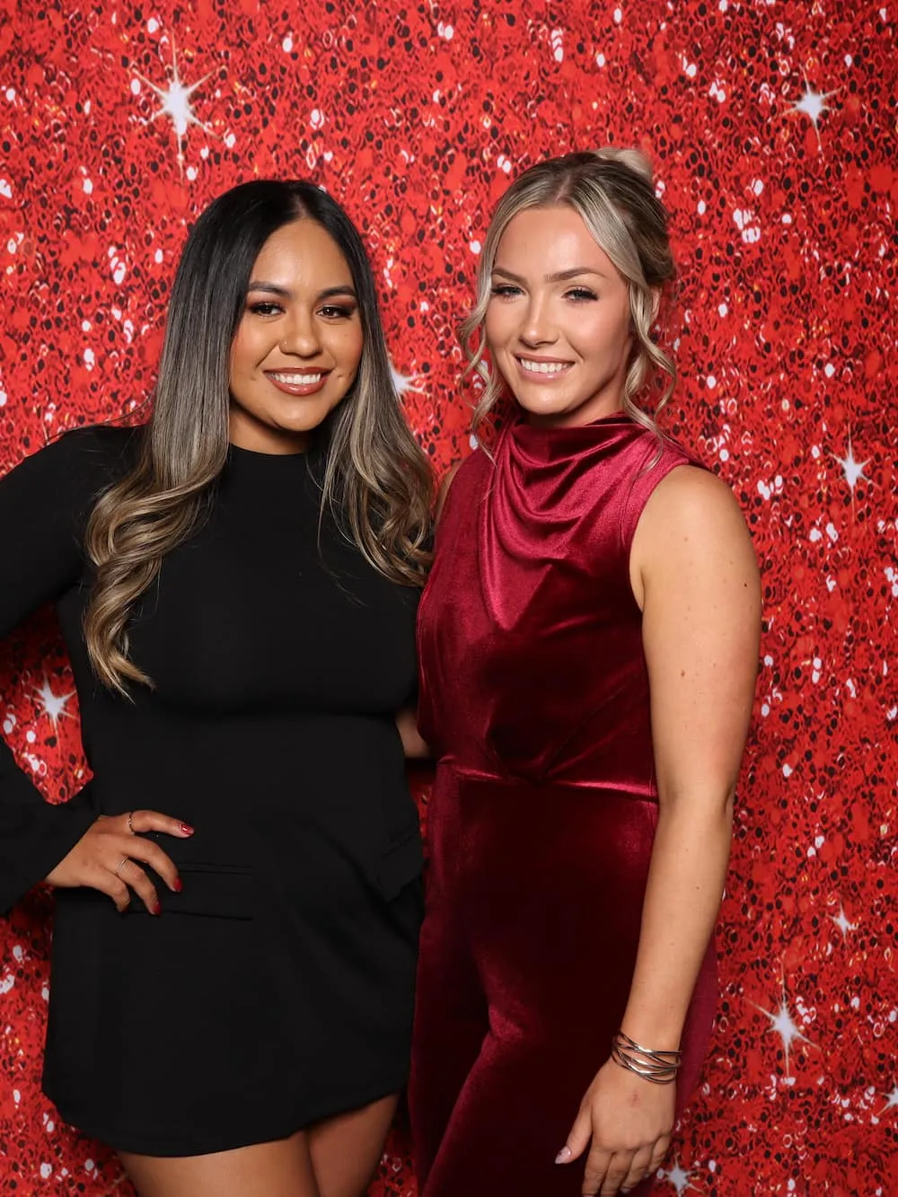 Two guests posing in front of a red sequin backdrop
