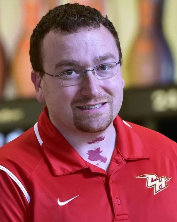 Portrait of Mike Blakeney, smiling and holding a bowling ball, standing in front of a softly lit bowling lane. Professional, approachable, and focused demeanor.