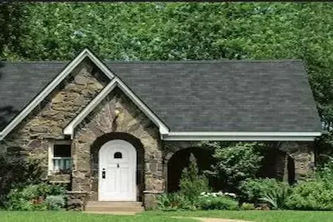 Stone cottage home with completed dark shingle roof installation by Coon Rapids Roofing Pros