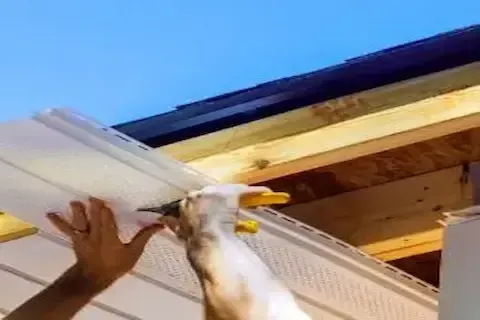 Worker installing white soffit panel under roofline eave in Coon Rapids