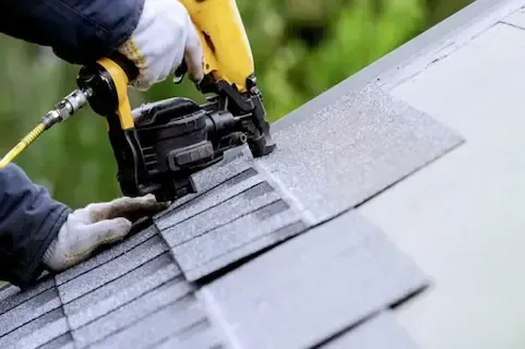 Roofer nailing down new asphalt shingles with a pneumatic nail gun during roof replacement in Coon Rapids