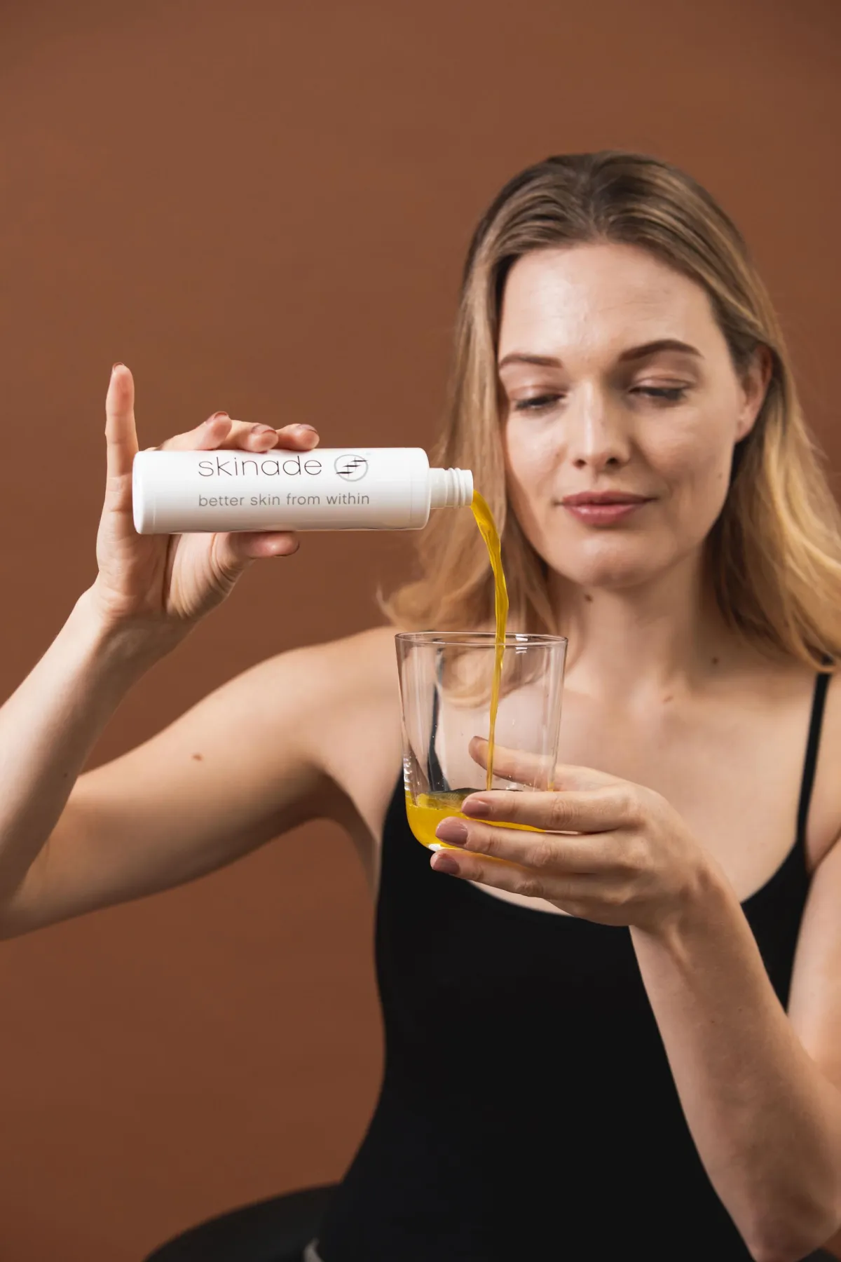 Woman pouring Skinade, drinkable collagen supplement, into glass