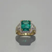 Emerald-cut emerald ring with diamond halo, baguette side stones, and dual-tone yellow and white gold setting by Montresor Infini.