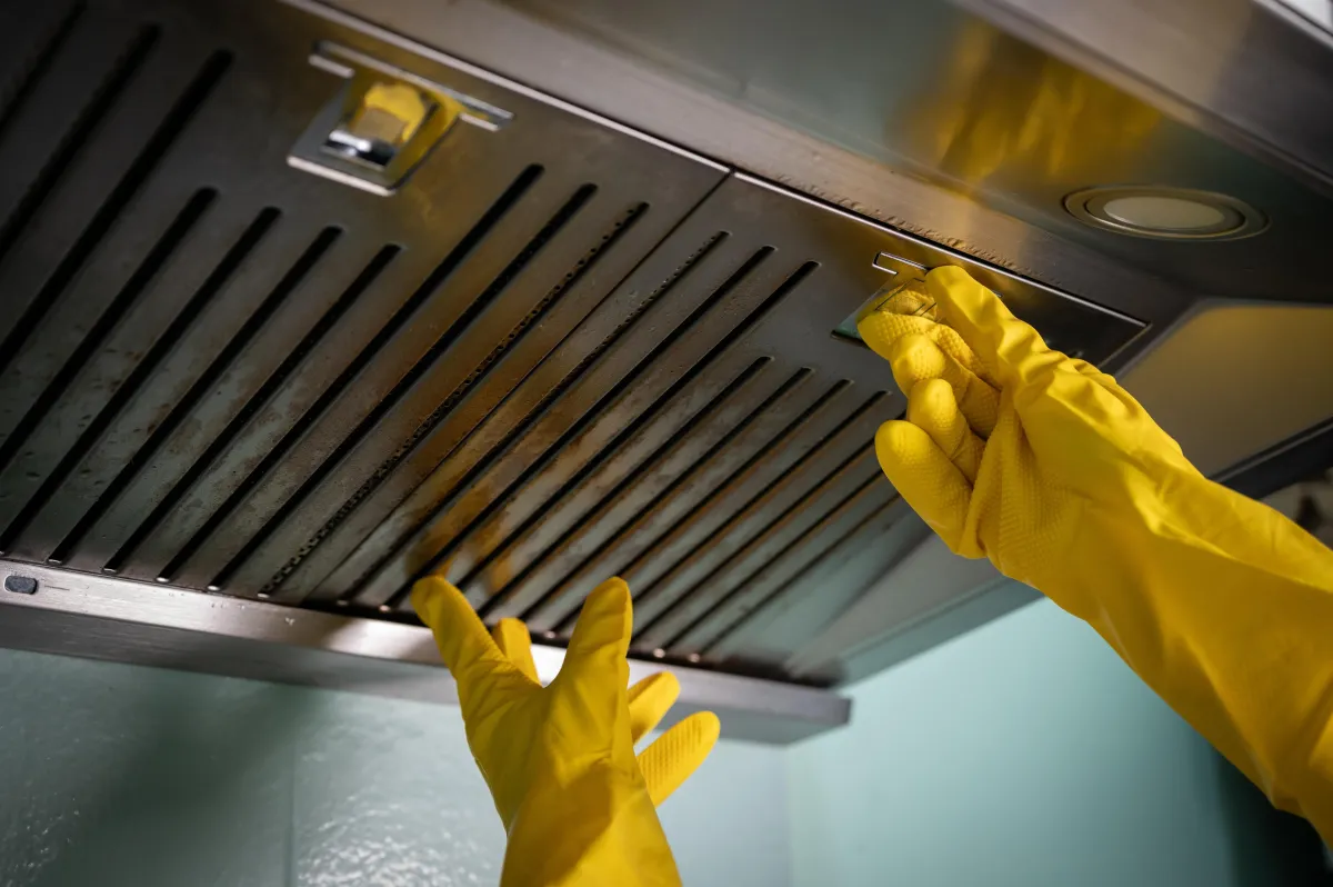 yellow gloved hands are preparing to clean a dirty kitchen hood