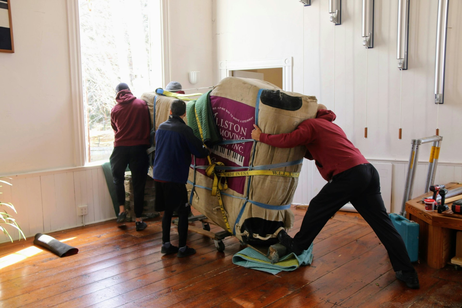 Movers wheeling a wrapped piano into a room - Blanco's Hauling and Handyman Service in San Bernardino