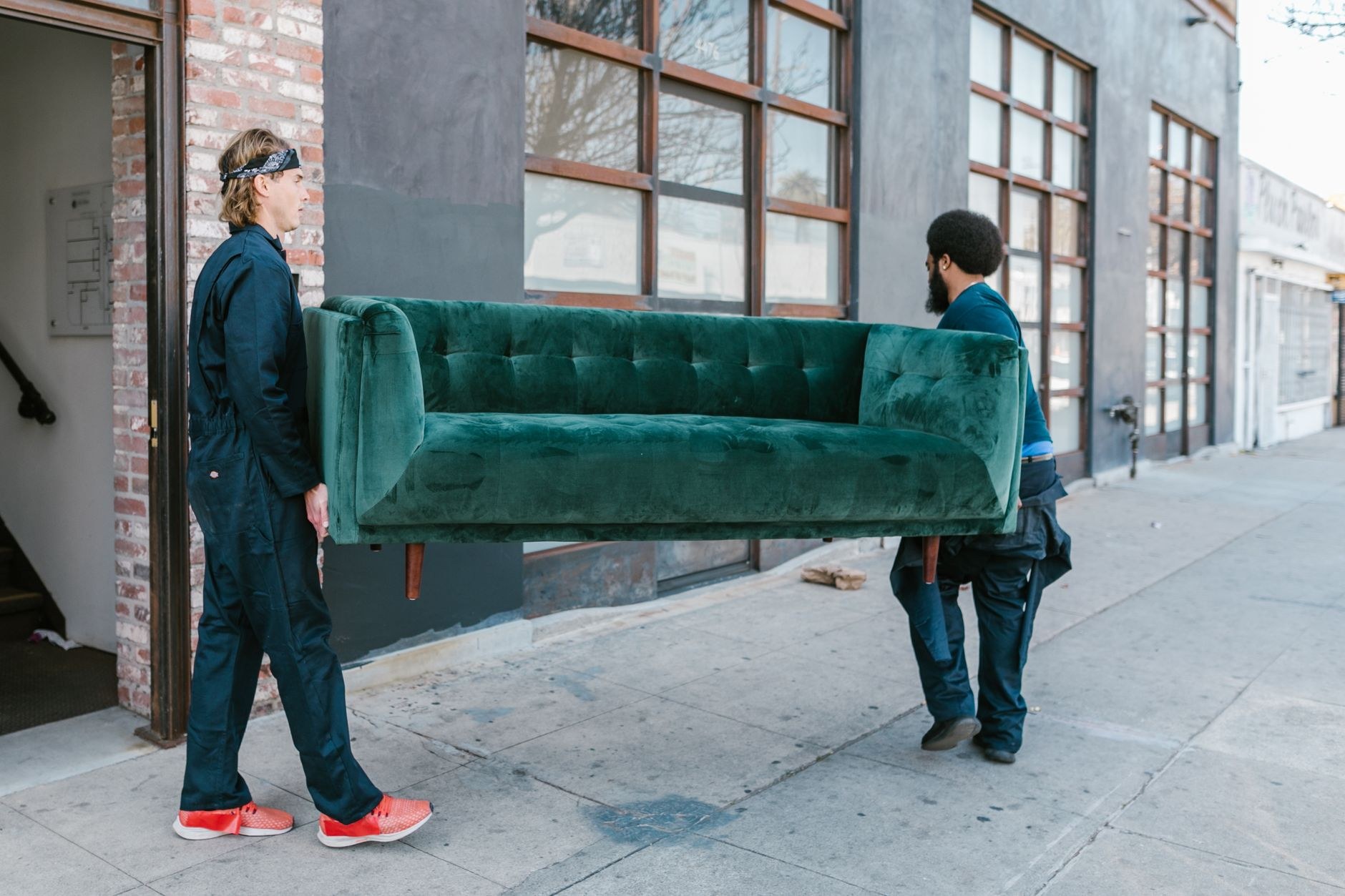 Two movers carrying a green velvet sofa outside - Blanco's Hauling and Handyman Service in San Bernardino