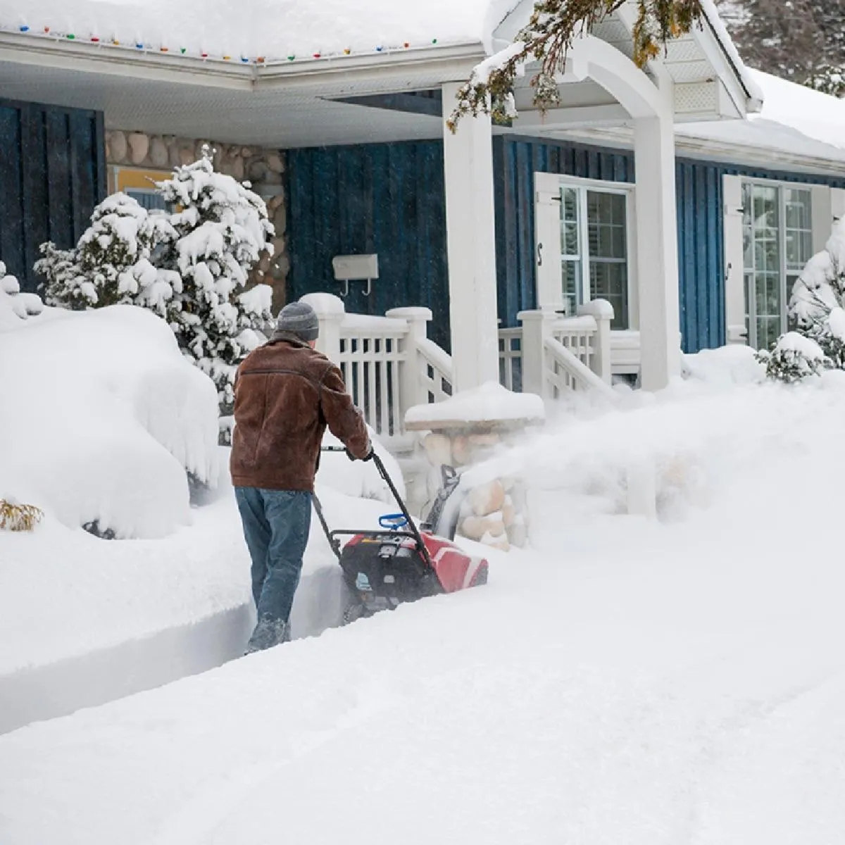 A man removing snow from the outside of his house using a small snow removing machine.
