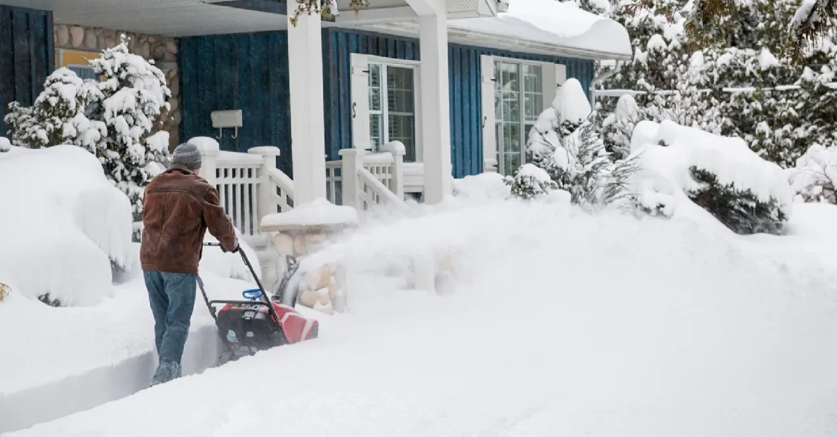 A man clearing snow from the side walk of a house. 
