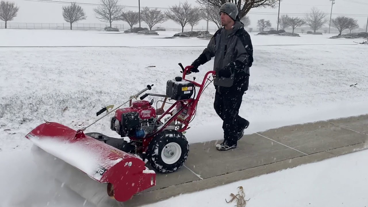 A man clearing snow from the sidewalk using heavy and advanced machine.