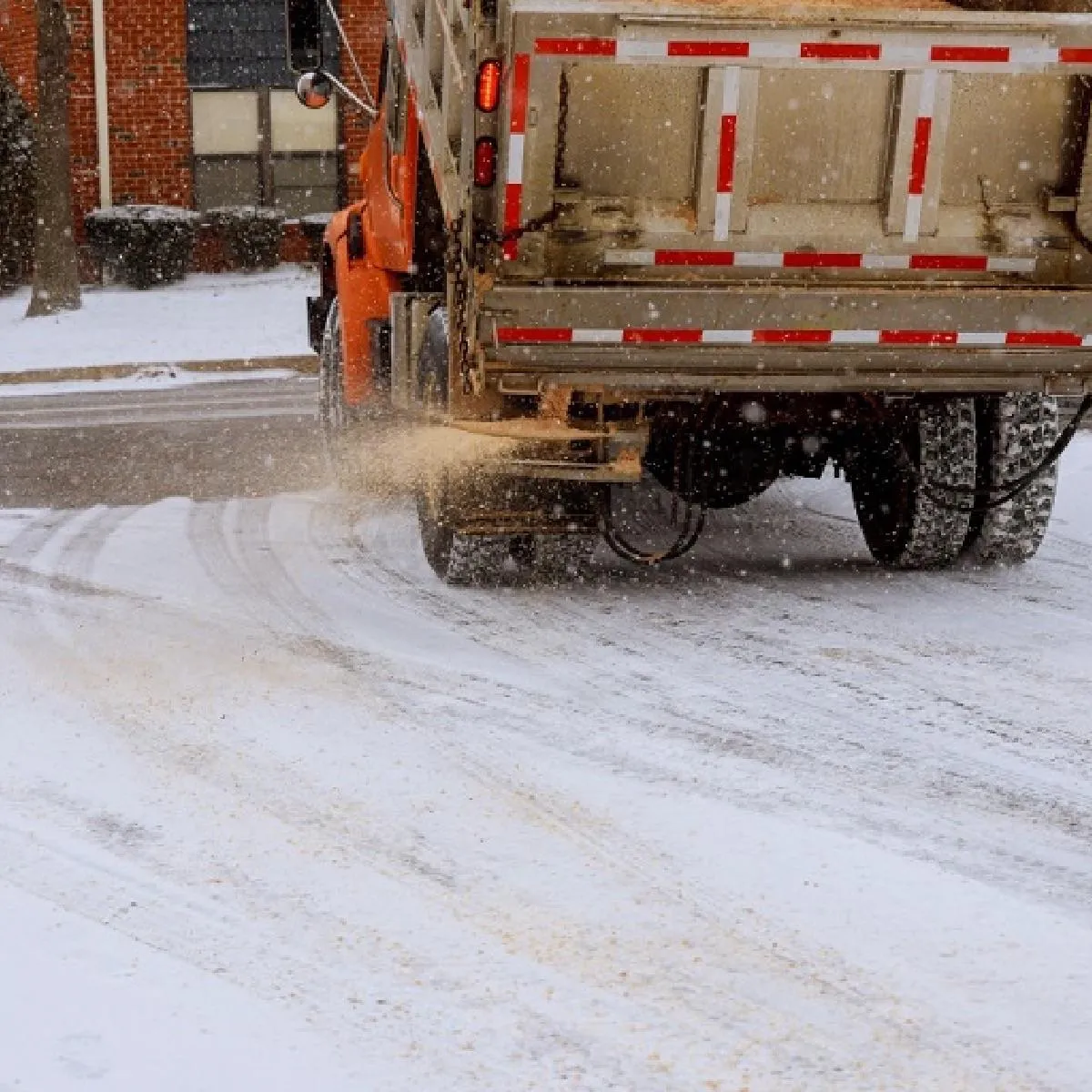 A truck sprinkling sand on a road full of snow to prevent Icing
