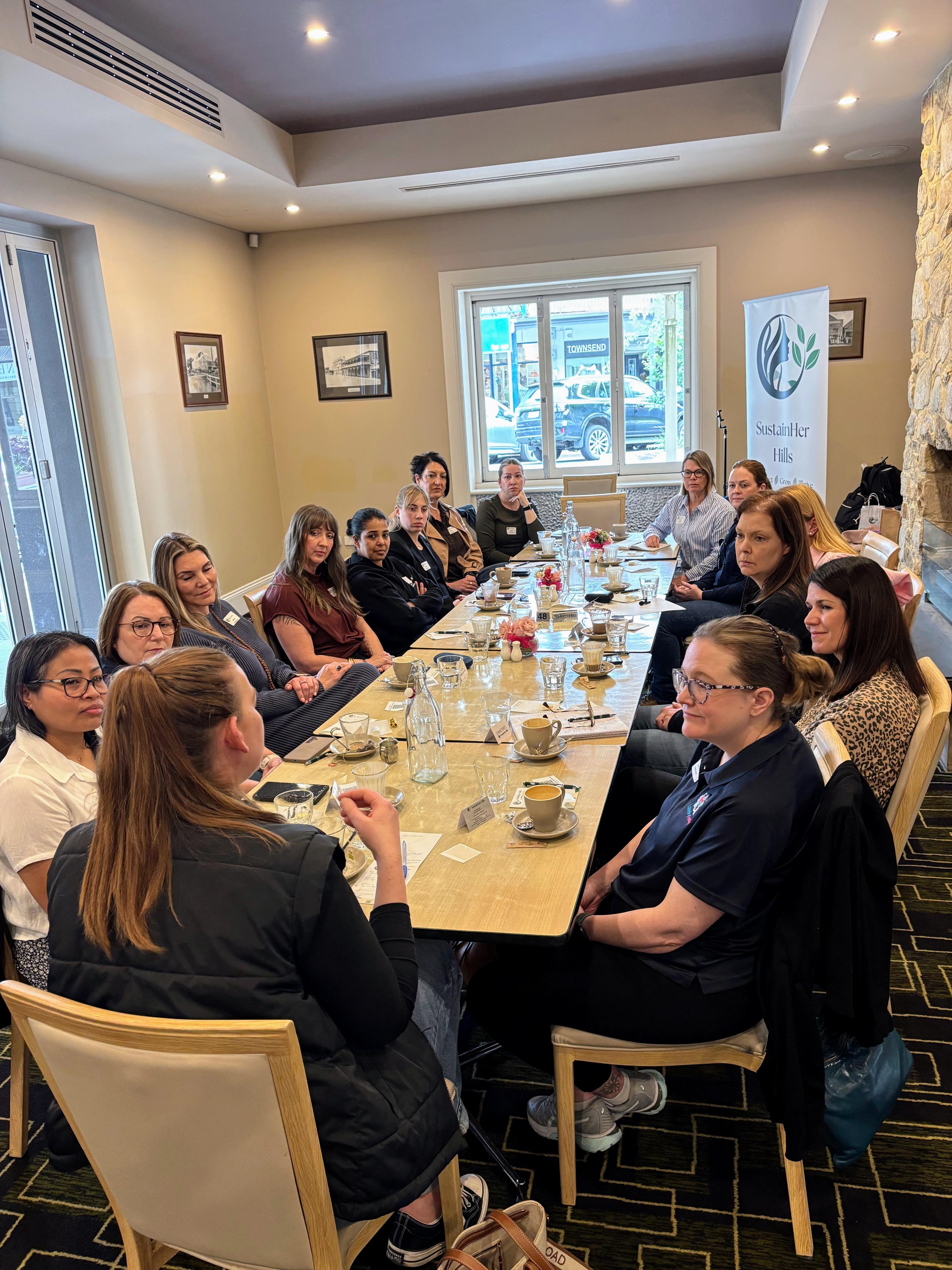 A resource table filled with business books, digital tablets, and branded notebooks, set up at an event. The materials are neatly arranged, and a hand is reaching for a guide, symbolizing access to valuable tools.