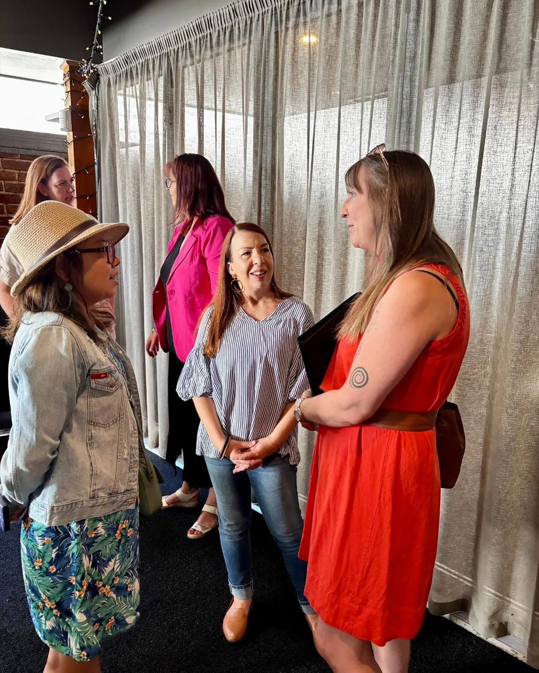 A vibrant networking event with small business owners exchanging business cards and laughing, set in a modern venue with string lights and plants. The group is diverse, and the mood is friendly and energetic.