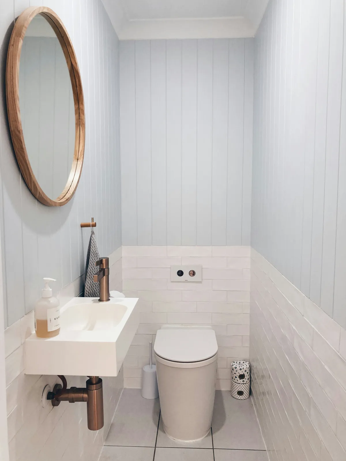 white and baby blue toilet room with small skink and round mirror