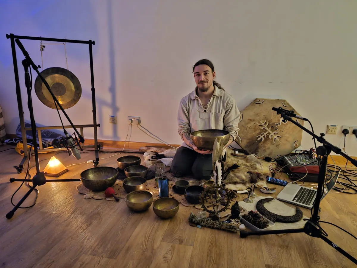 Cory Condor, the founder of Sunyata Sound Healing, is pictured sitting on the floor surrounded by sound bowls.