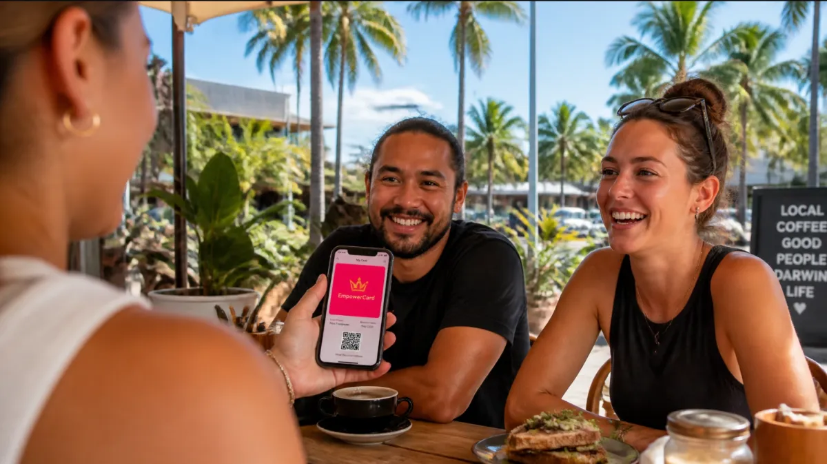 A group of diverse friends smiling and laughing at a sun-drenched outdoor Darwin cafe, with one person holding a phone showing the digital EmpowerCard app.